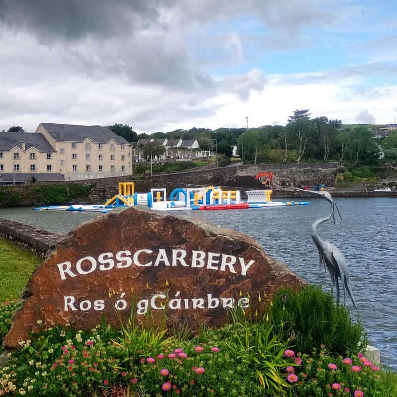 Stone with the name of the town Rosscarbery in English and Irish and the inflatable water park in the background