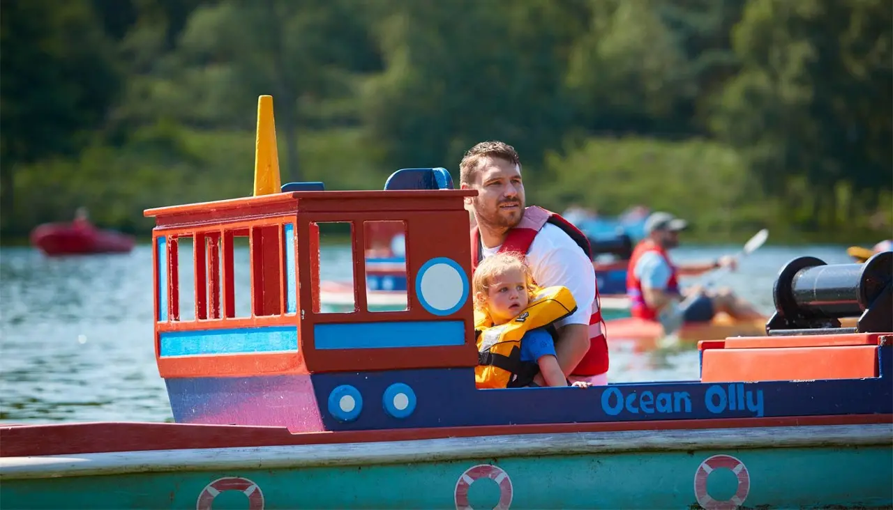 Two young children seated and steering their Mini Captain ride with an adult beside them on a sunny day in West Cork.