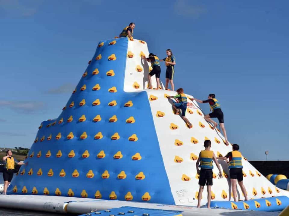 Group of people climbing the 9m tall "iceberg" obstacle in the Rosscarbery's inflatable water park