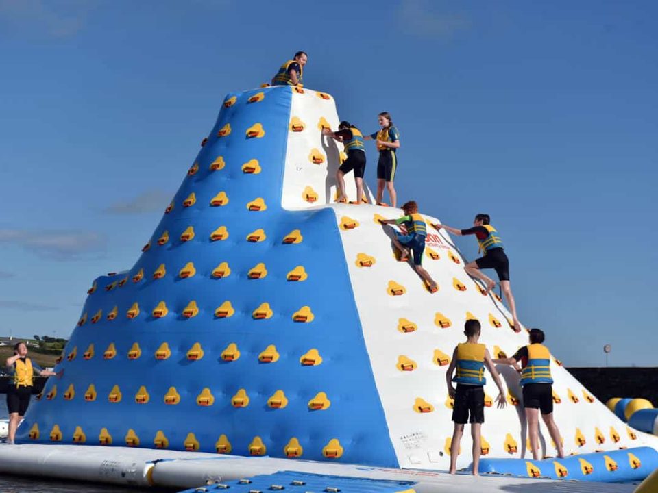 Group of people climbing the 9m tall "iceberg" obstacle in the Rosscarbery's aqua park