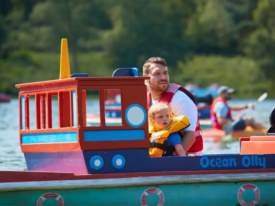 Two young children seated and steering their Mini Captain ride with an adult beside them on a sunny day in West Cork.